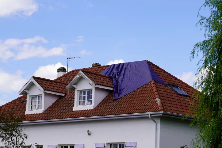 Image of a home with a damaged roof from a hail storm, covered with a tarp
